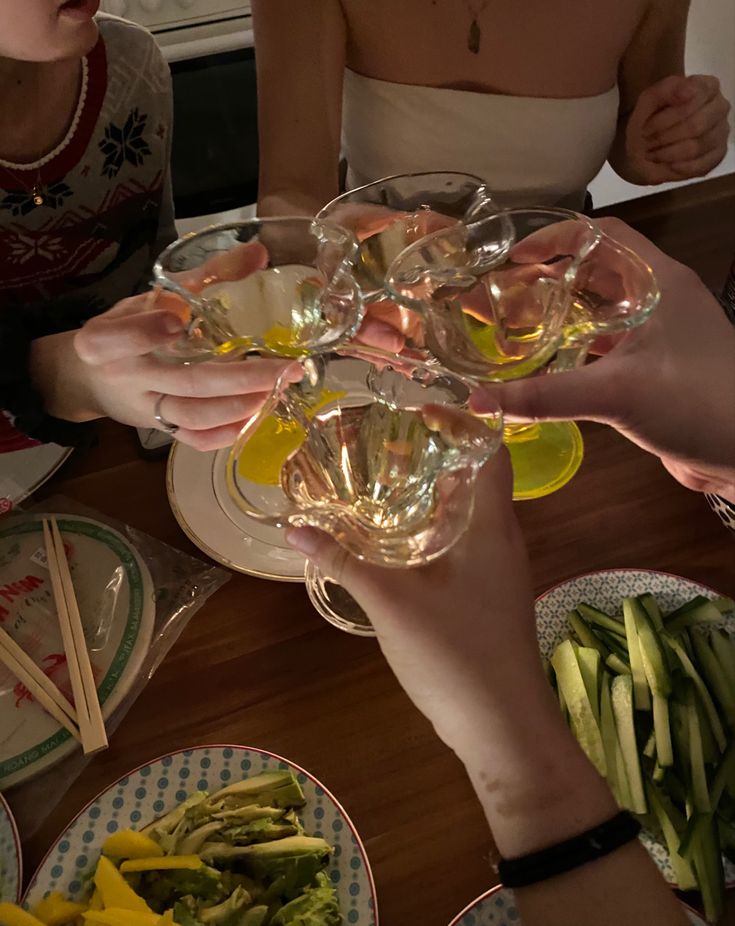 several people toasting with wine glasses and vegetables on the table in front of them