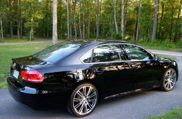 a black car is parked on the side of the road in front of some trees