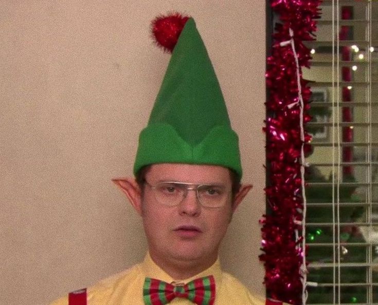 a man wearing a green elf hat and bow tie in front of a christmas tree