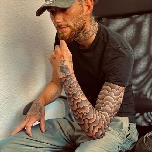 a man with tattoos on his arm sitting down and holding his hand to his chin