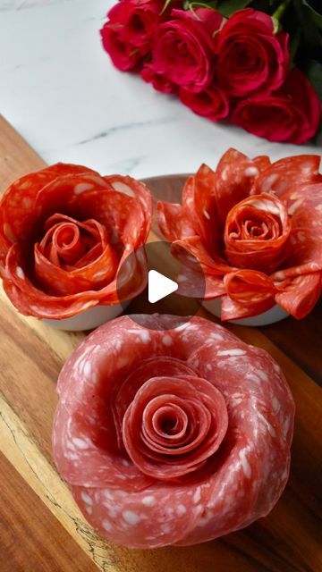 three red flowers sitting on top of a wooden table next to a bowl with meat