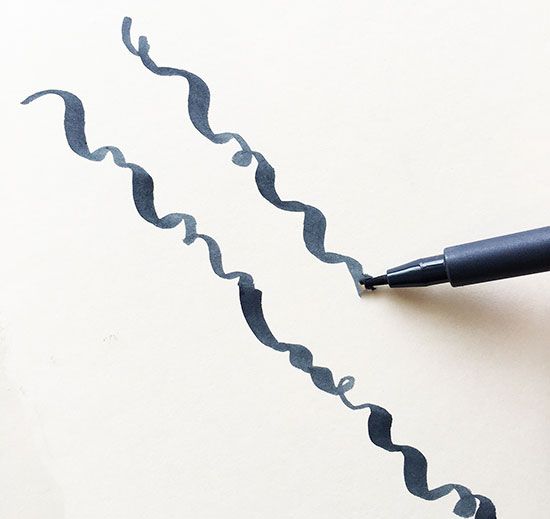 a black pen is writing on paper with wavy lines drawn across the top and bottom