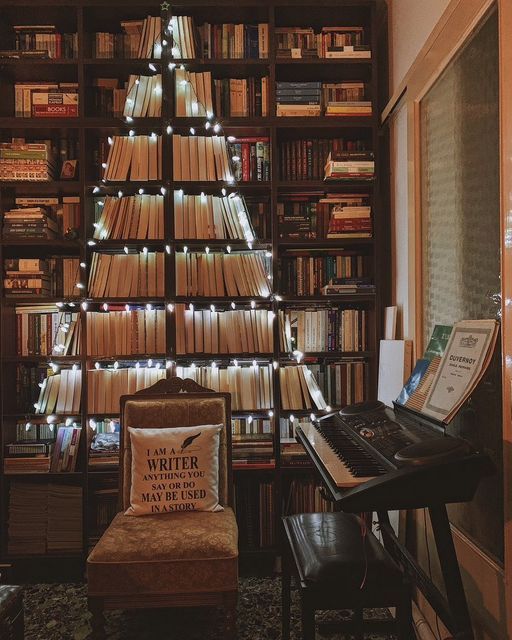 a christmas tree made out of books in a living room with a piano and chair