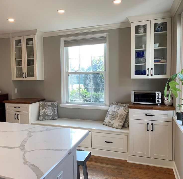 a kitchen with white cabinets and marble counter tops in front of a window that is open to the outside