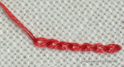 an orange thread is on top of a white piece of fabric with red stitching