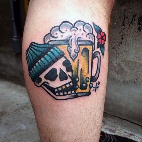 a skull with a hat and beer mug tattoo on his leg is seen in this image