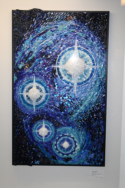 an abstract painting hanging on the wall in a white walled space with blue circles and stars