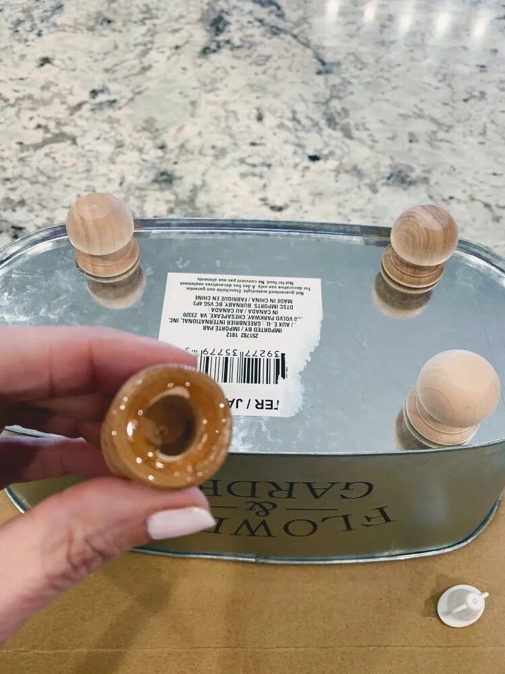 a person holding a donut in front of a metal tray with wooden knobs