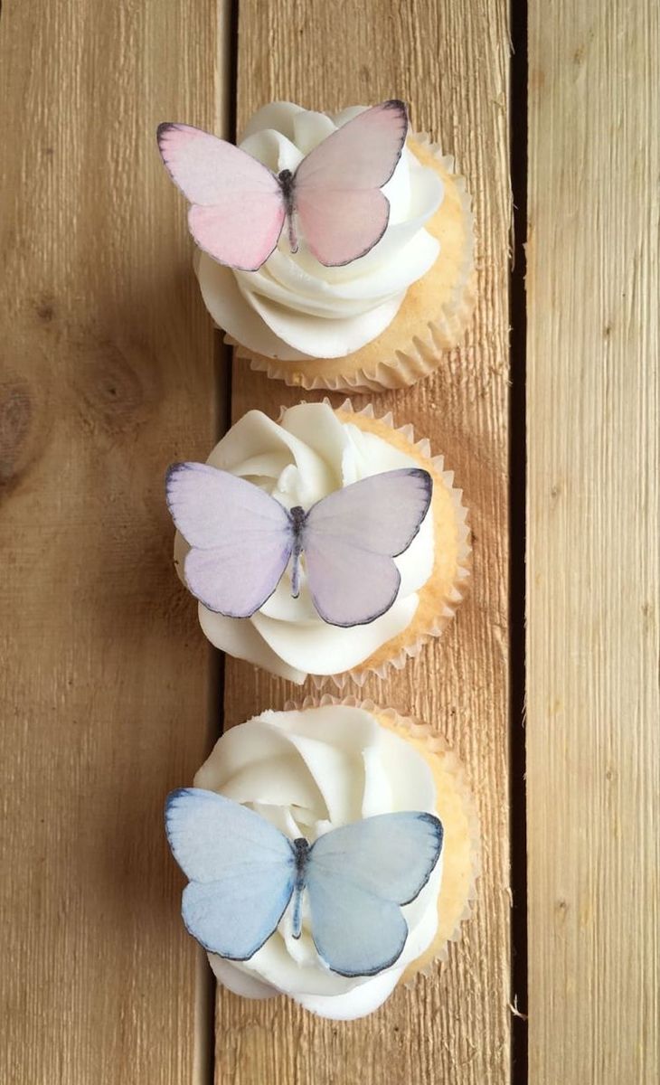 three cupcakes with butterflies on them sitting on top of a wooden table next to each other