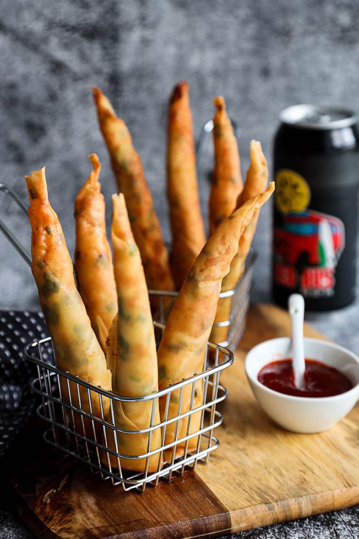 some food is in a metal basket on a wooden cutting board next to a can of ketchup