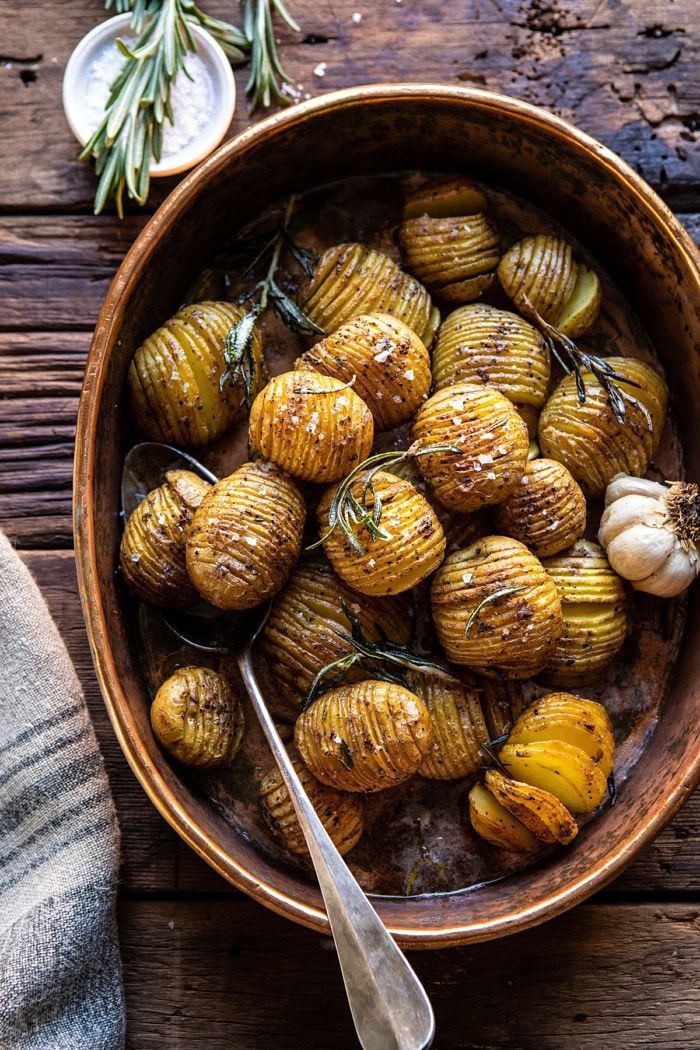 a wooden bowl filled with potatoes and garlic next to a spoon on top of a table