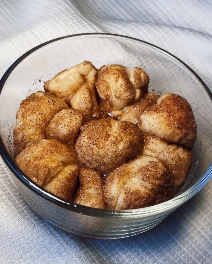 a glass bowl filled with cinnamon rolls on top of a white tablecloth covered table