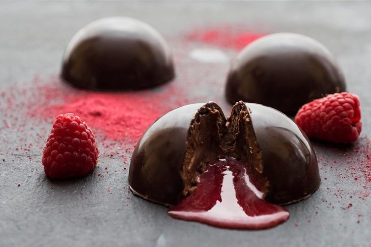 three chocolates with raspberries on the side and one broken in half sitting on a table