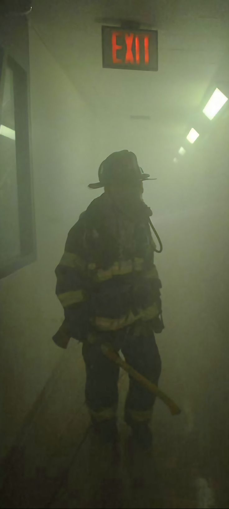 a fireman standing in the fog with his back turned to the camera and holding a stick