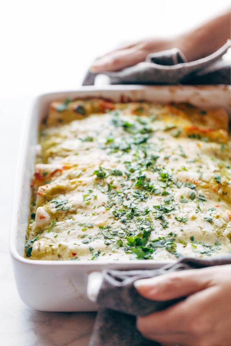 a person holding a casserole dish with cheese and vegetables