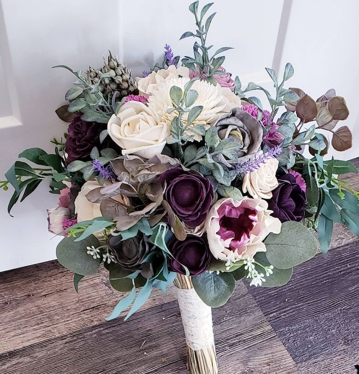 a bridal bouquet with purple and white flowers on a wooden floor in front of a door