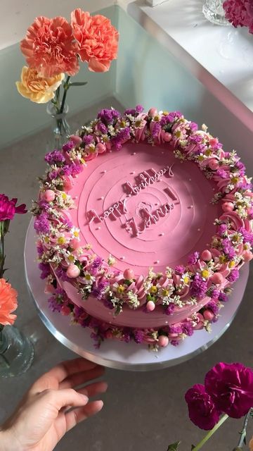 a pink birthday cake with flowers around it