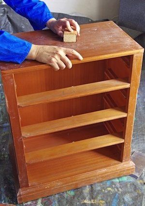 a person with their hand on the top of a wooden bookcase that is being worked on