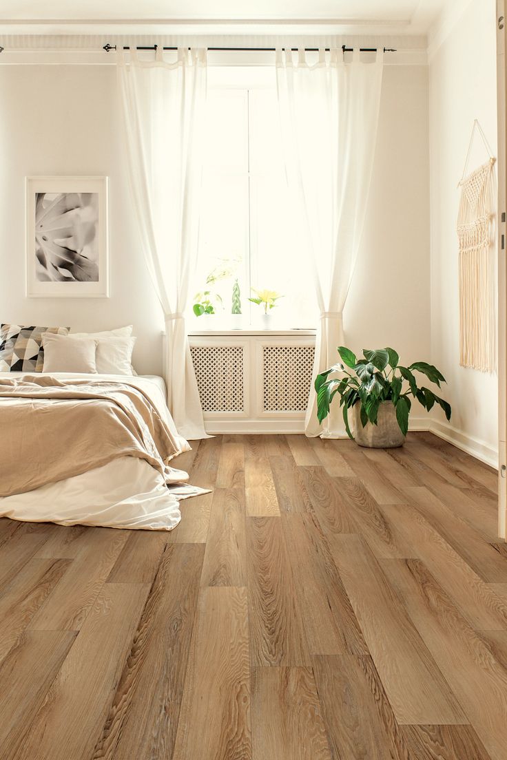 a bedroom with wood flooring and white curtains on the window sill is shown