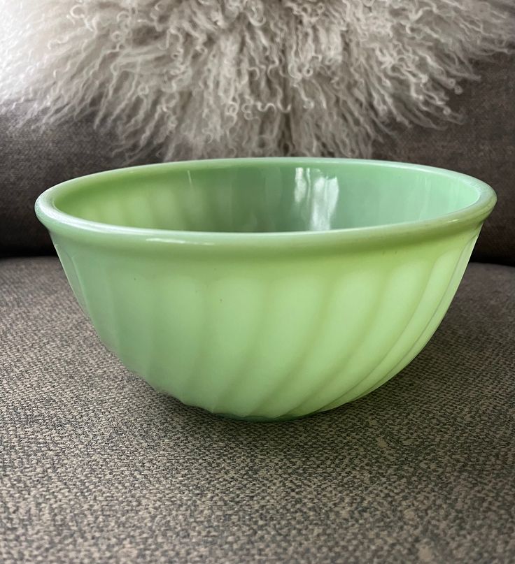 a green bowl sitting on top of a couch next to a white fluffy animal pillow