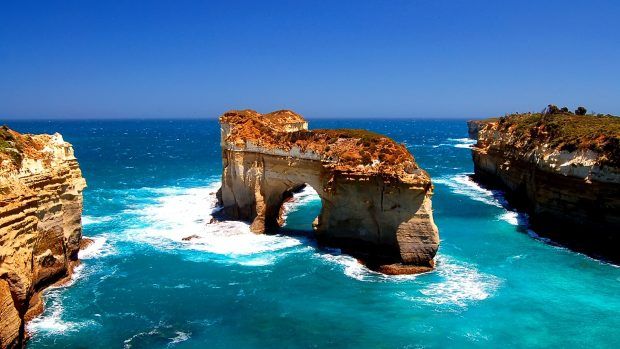 two large rocks sticking out of the ocean next to each other on top of a cliff