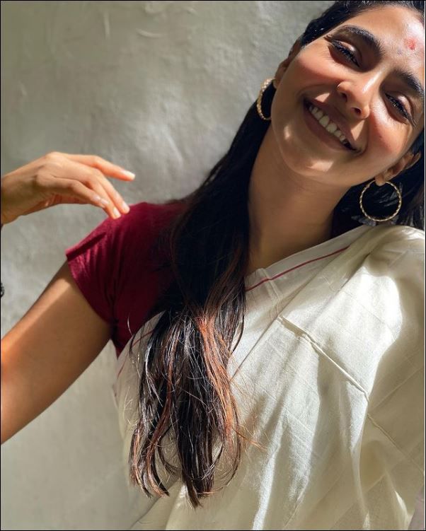 a woman is smiling and wearing a white sari with gold hoop earrings on her head