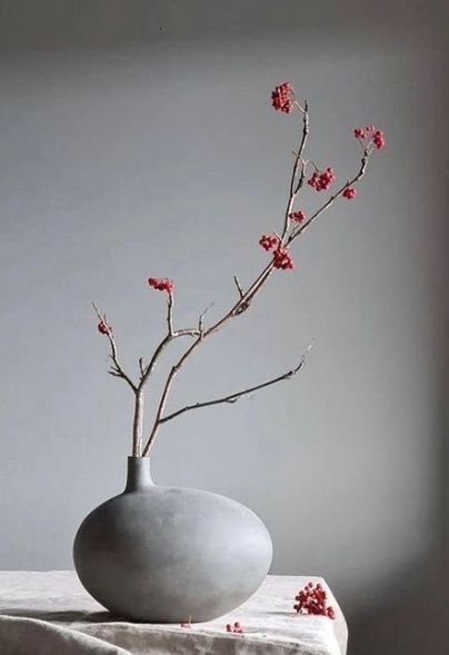 a vase with red flowers in it sitting on a white table cloth next to a window