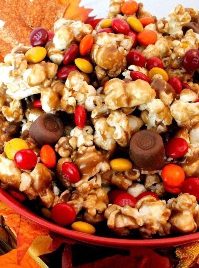 a red bowl filled with candy corn and candies on top of autumn leaves next to an orange maple leaf