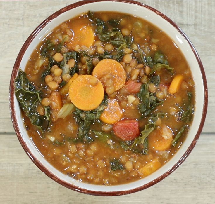 a bowl of soup with carrots, beans and spinach on the top is sitting on a wooden table