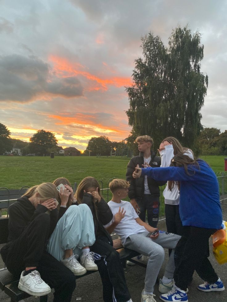 a group of people sitting on top of a park bench next to each other at sunset