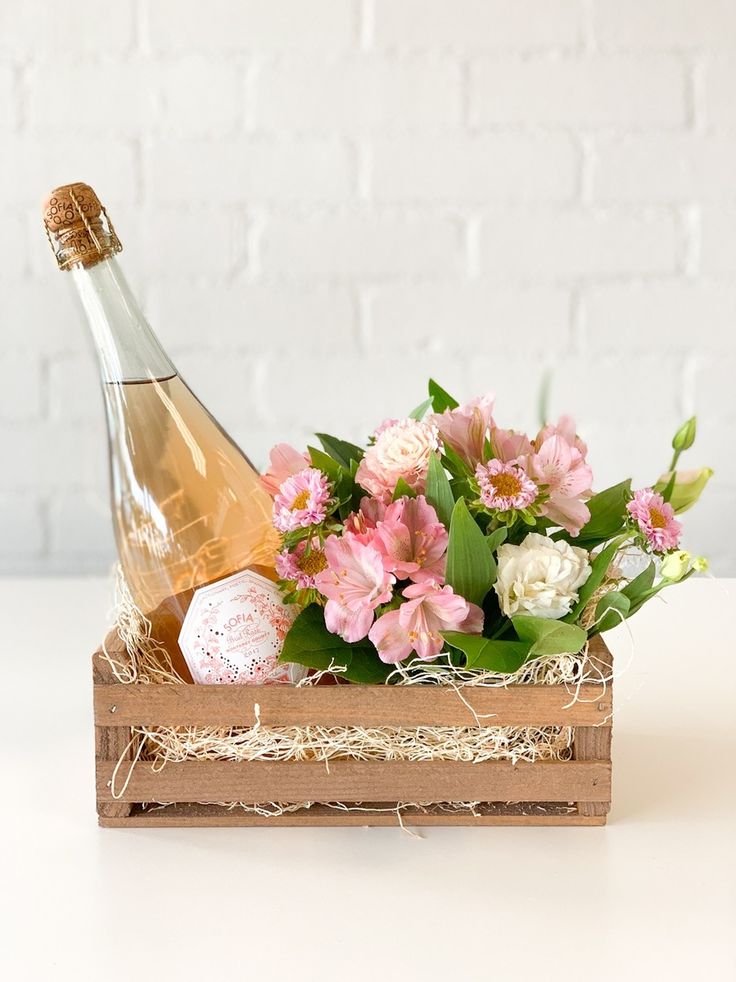 a bottle of champagne and flowers in a wooden crate on a white table with straw