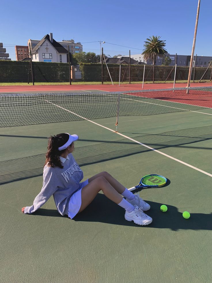 a woman sitting on the ground with a tennis racket and ball in her hand