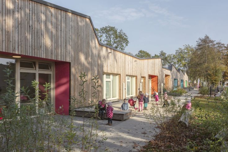 children are playing outside in the courtyard of an apartment building with wooden siding and red doors