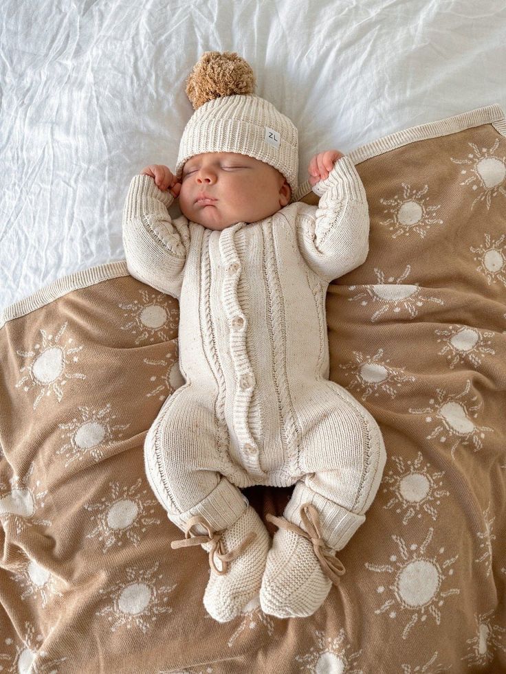 a baby laying on top of a bed wearing a knitted hat