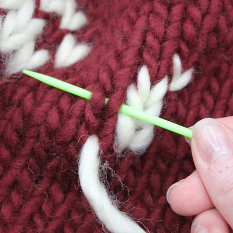 someone is crocheting the stitches on a red knitted sweater with green needles