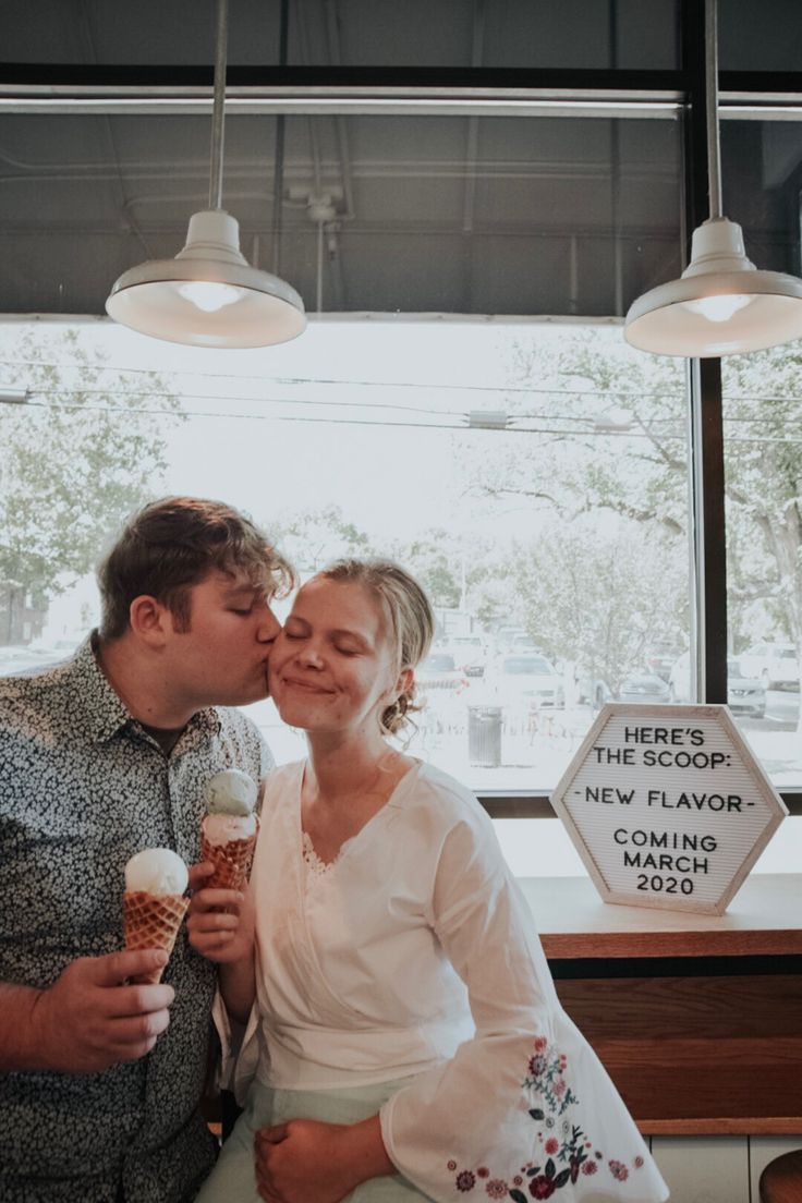 a man and woman kissing while holding ice cream cones in front of a large window