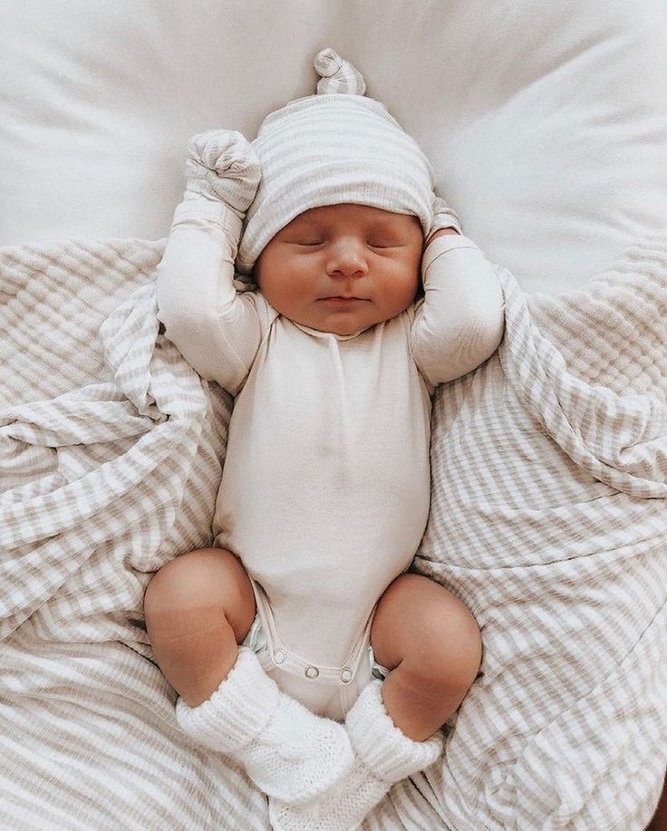 a baby laying on top of a bed wearing a white hat