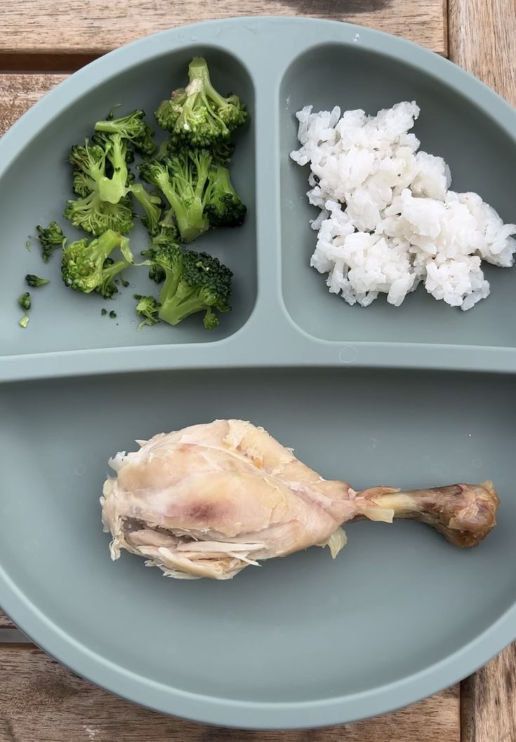 a plate with rice, broccoli and chicken on it sitting on a wooden table