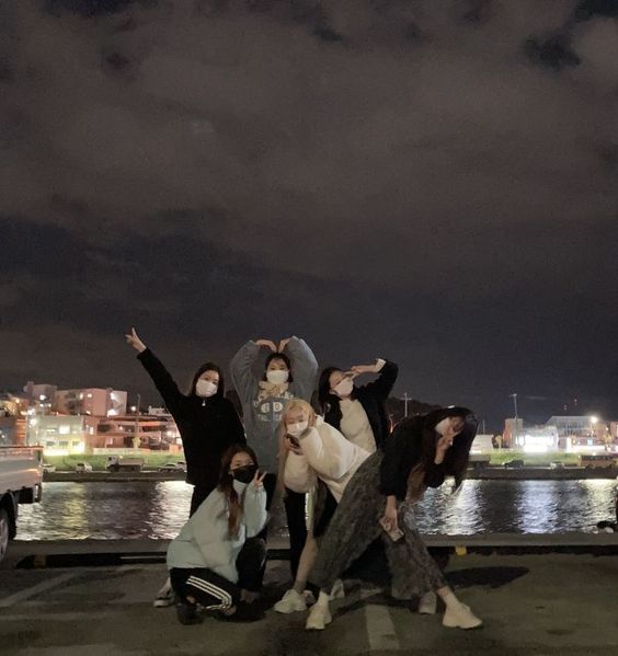 four people posing for a photo in front of the water at night with their arms up