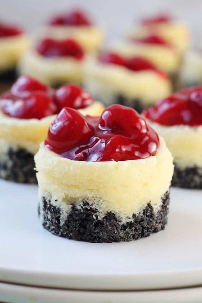 mini cheesecakes with cherries on top sitting on a white plate, ready to be eaten