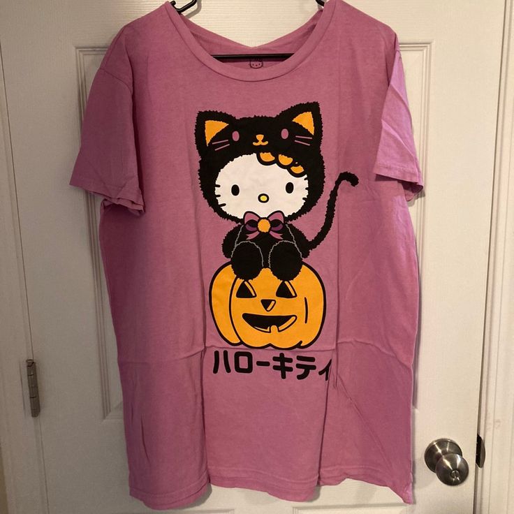 Hello Kitty Pumpkin T-Shirt Get Ready For Halloween Every Day With The Purr-Fect Tee! This Tee Features Hello Kitty Donning A Black Cat Costume And Sitting Atop A Jack-O'-Lantern. 100% Cotton Wash Cold; Dry Low Imported Pink Short Sleeve Top With Hello Kitty Print, Cute Pink T-shirt With Cat Print, Cute Pink Hello Kitty T-shirt, Pink Character Print Tops For Loungewear, Halloween Character Print Pink Top, Pink Hello Kitty Crew Neck T-shirt, Pink Hello Kitty Short Sleeve T-shirt, Pink Short Sleeve Hello Kitty T-shirt, Pink Halloween Graphic Tee