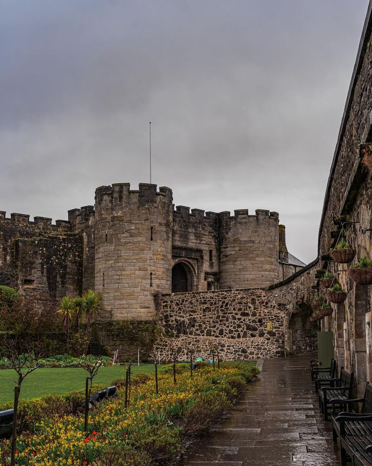 an old castle with flowers and benches in the foreground, on a rainy day