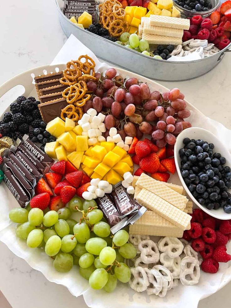 two trays filled with assorted fruit and crackers on top of a table