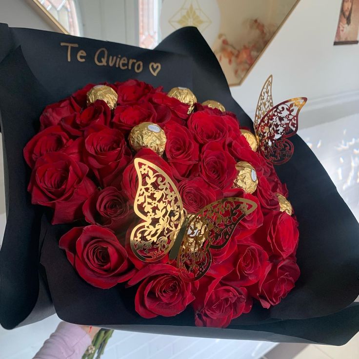 a bouquet of red roses and butterfly brooches in a black box with the words te guero on it