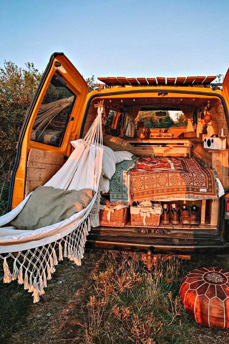 the back end of an orange van filled with luggage and blankets, sitting in a field