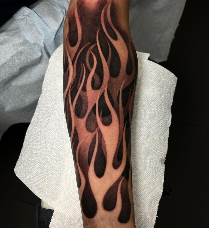 a man with a black and grey tattoo on his arm that has flames coming out of it