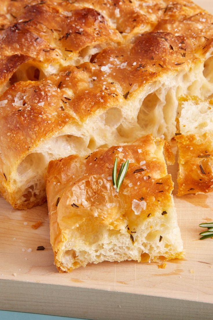 a piece of bread that has been cut in half on a cutting board with rosemary sprigs