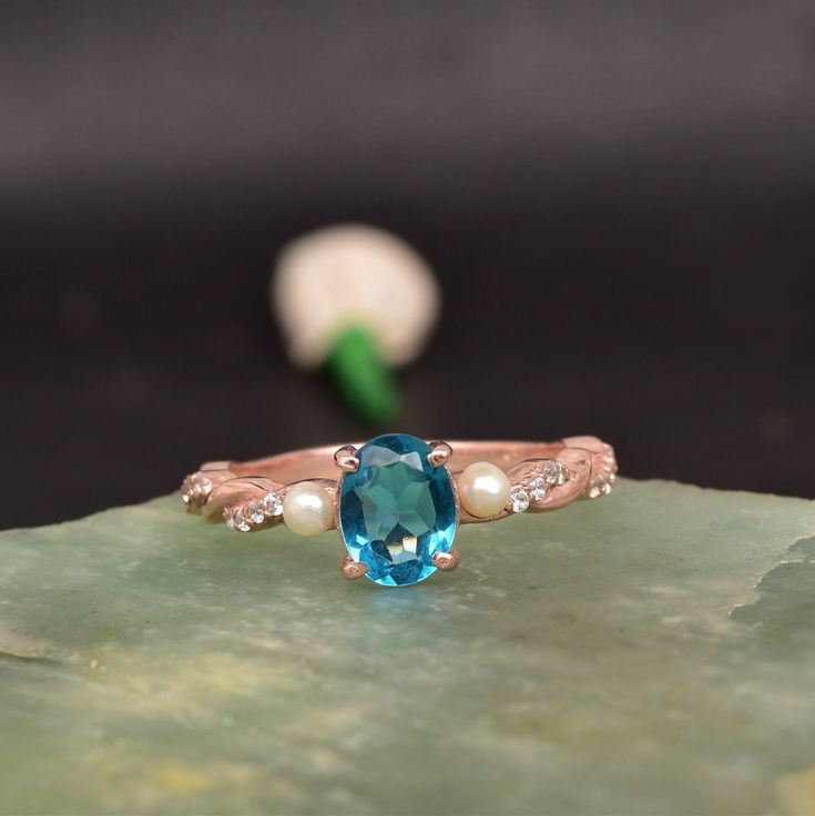 a close up of a ring with a blue stone and pearls on the side, sitting on top of a leaf