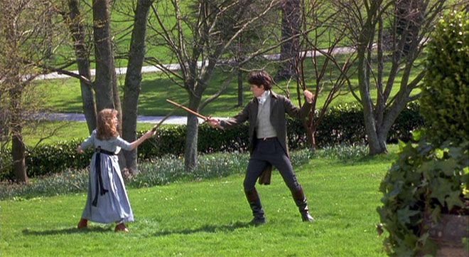 a man and woman in period dress playing with a stick on the grass next to some trees