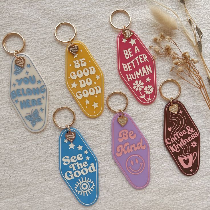 six keychains with different sayings on them sitting next to some dried flowers